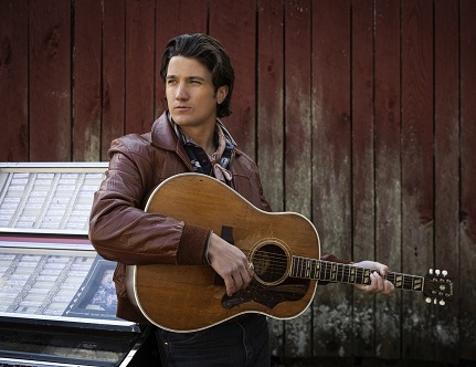 Photo of Drake Milligan holding a guitar next to a jukebox